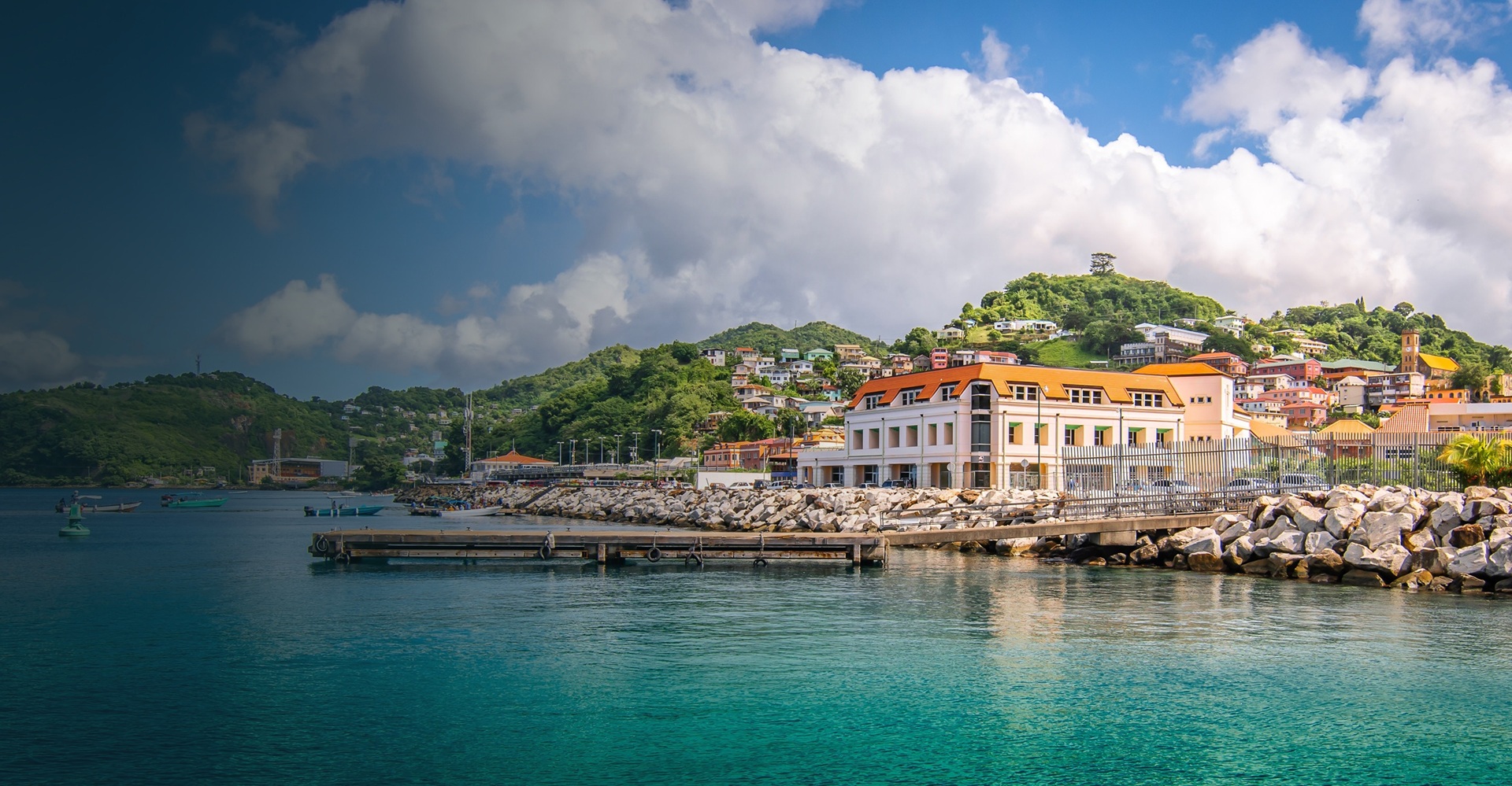 Waterfront of St George’s, Grenada, with colourful hillside houses, a stone harbour wall and turquoise water
